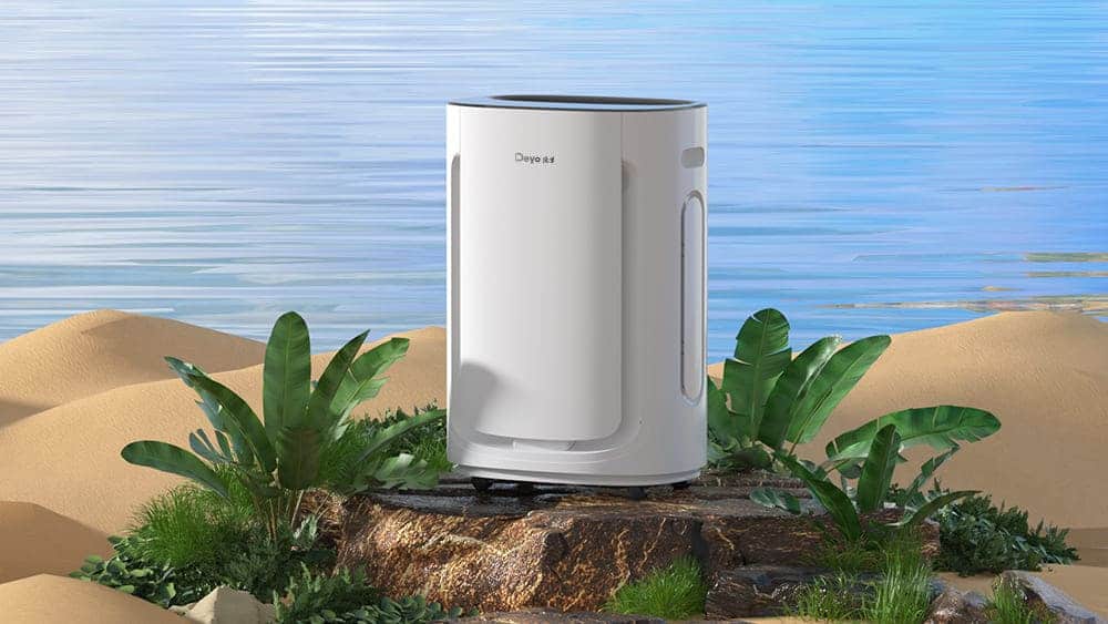 A portable dehumidifier on a rocky outcrop surrounded by sand and tropical plants, with a serene lake in the background.