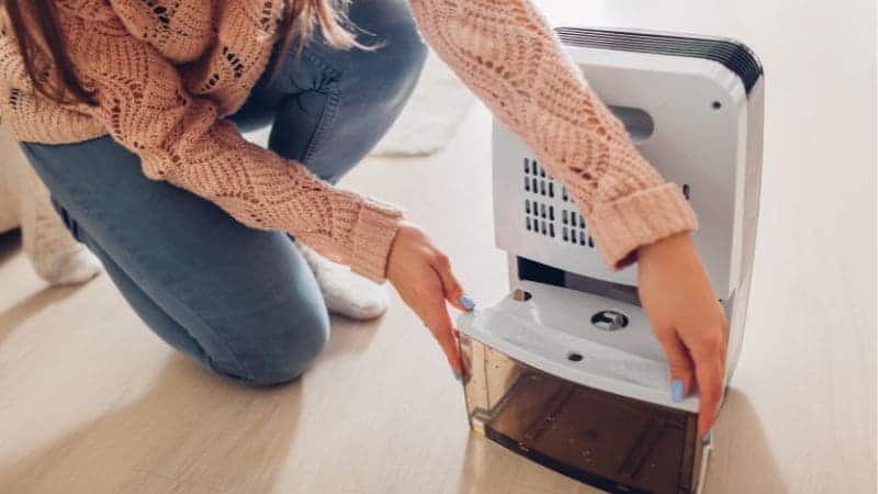 Een vrouw in een roze trui vervangt het filter van een luchtontvochtiger in een lichte kamer.